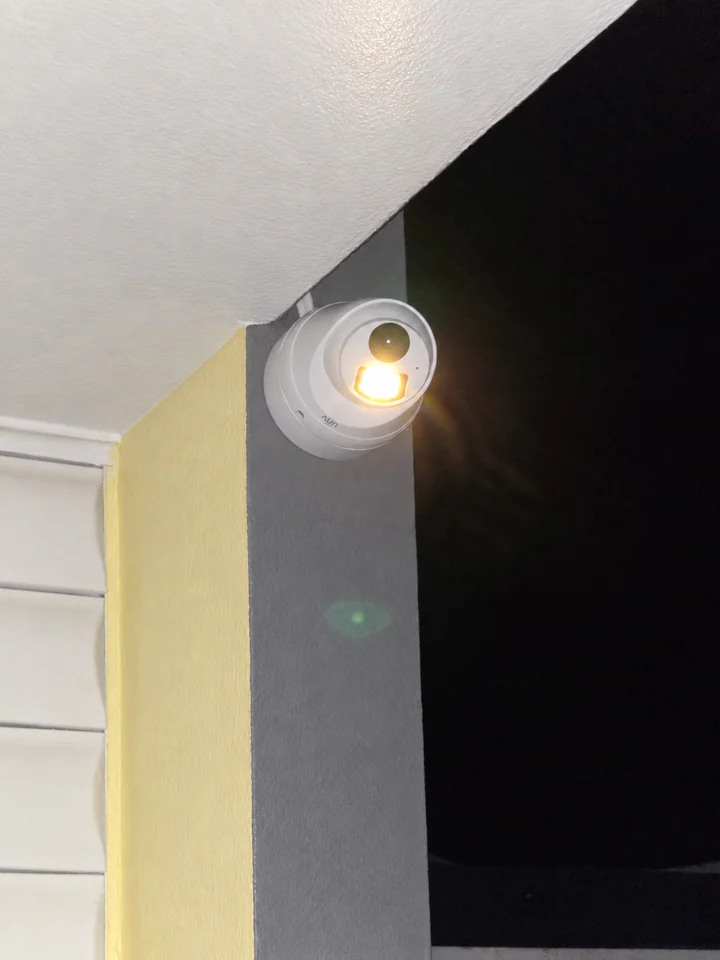 Cámara exterior en una columna bajo el alero, de noche y con su iluminación auxiliar encendida.
