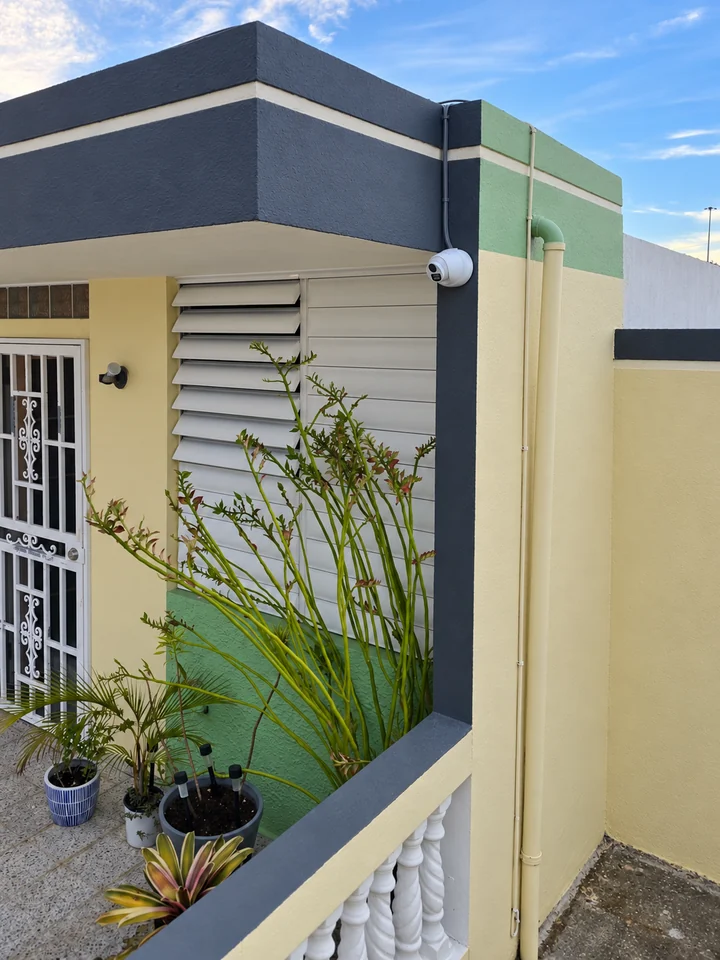 Cámara exterior montada en una columna gris de la fachada residencial, con canalización visible hacia el techo.